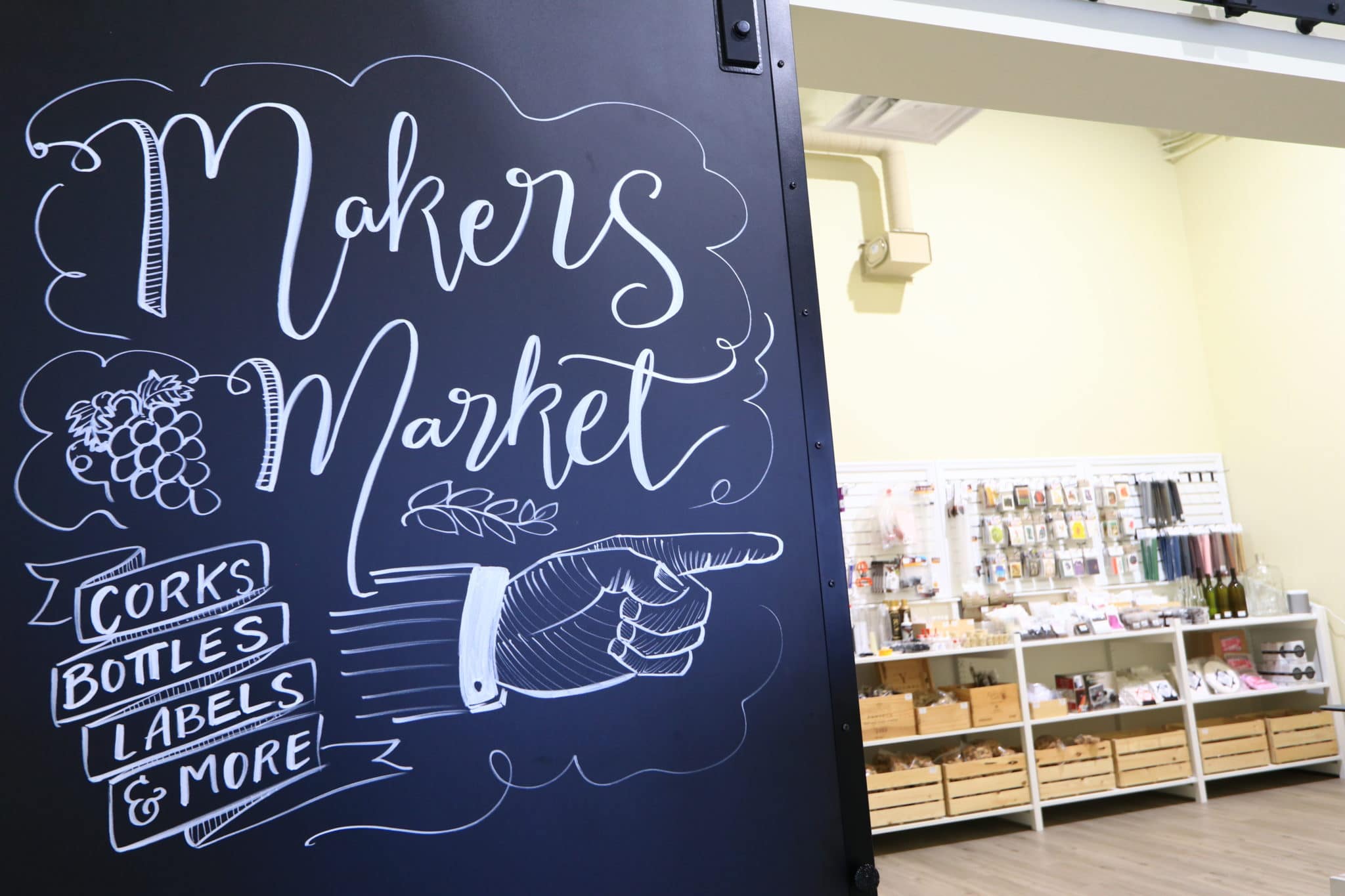 Maker's Market graphic on chalk door with wine making equipment in background